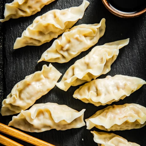 Steamed dumplings, or gyoza, arranged on a dark plate with a small bowl of soy sauce and chopsticks.