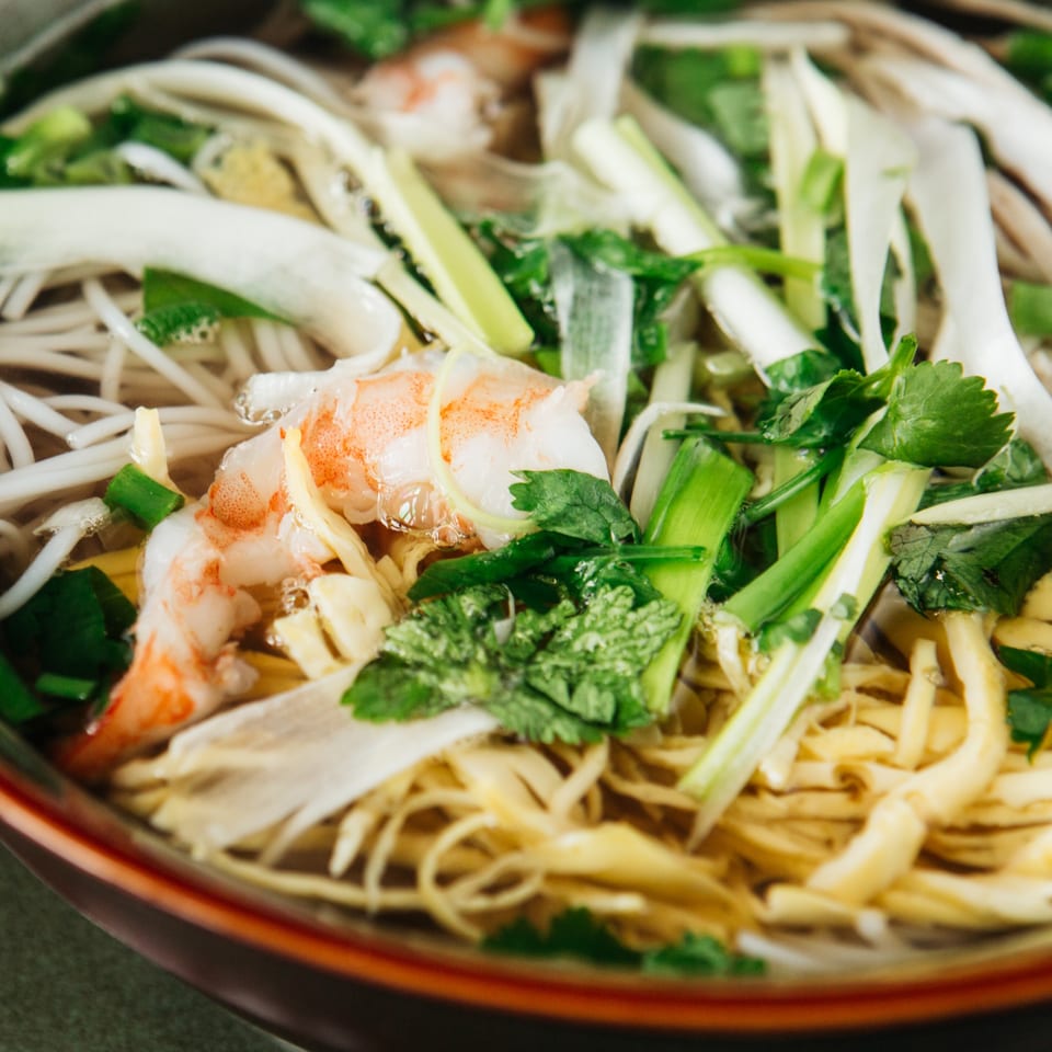 Close-up of Vietnamese pho with shrimp, noodles, green onions, and cilantro in a bowl.