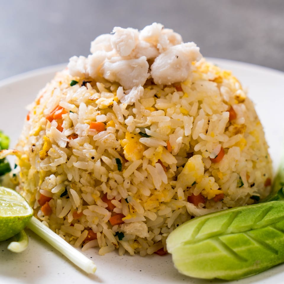 Crab fried rice with lime, green onion, and carved cucumber on a white plate.