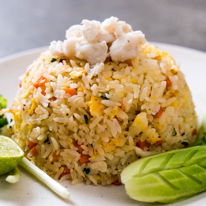 Crab fried rice with lime, green onion, and carved cucumber on a white plate.