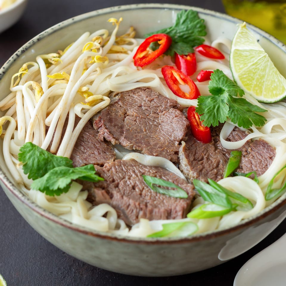 A close-up of Pho Tai's Vietnamese pho with beef, noodles, bean sprouts, chili, and lime.