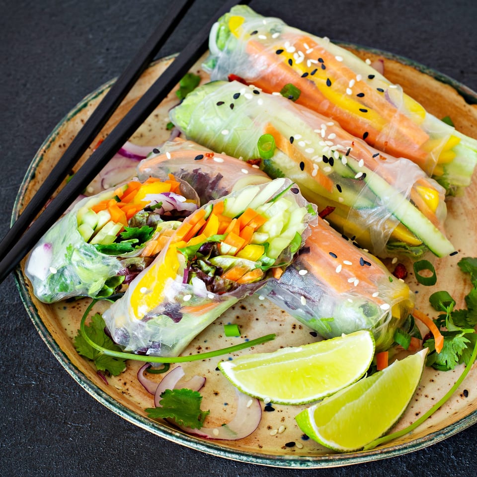 Fresh Vietnamese spring rolls with colorful vegetables, sesame seeds, and lime wedges on a plate.