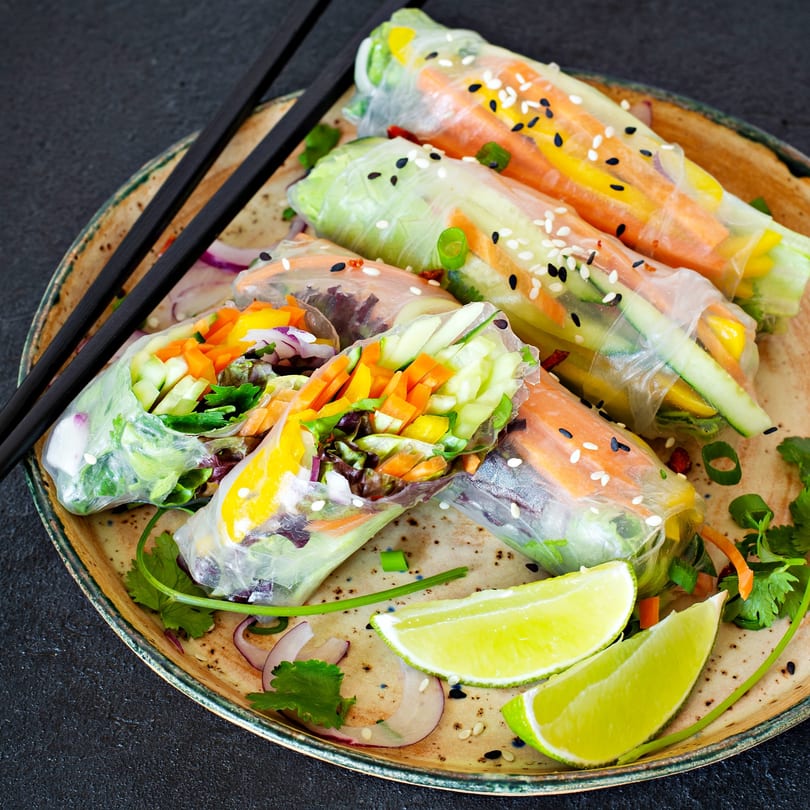 Fresh Vietnamese spring rolls with colorful vegetables, sesame seeds, and lime wedges on a plate.