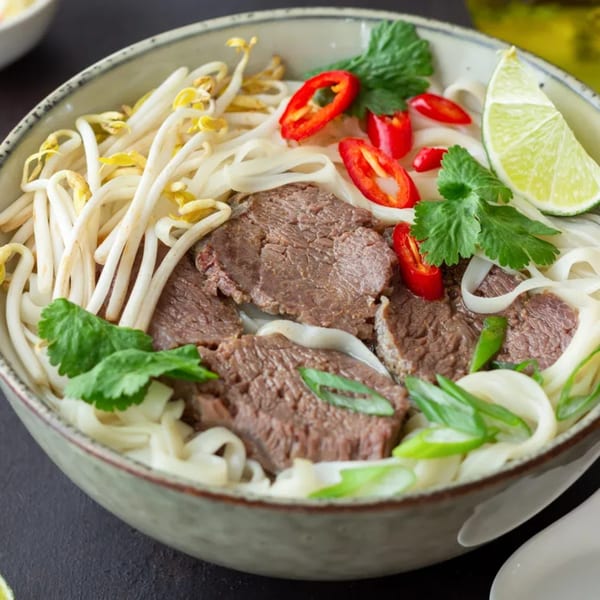 A bowl of Pho Tai with beef, noodles, bean sprouts, chili, cilantro, and a lime wedge.